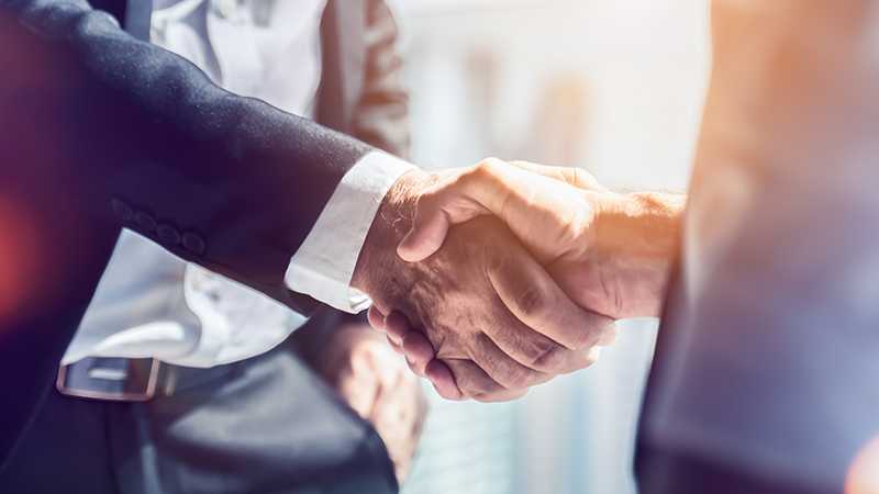 Two people wearing suits shaking hands.